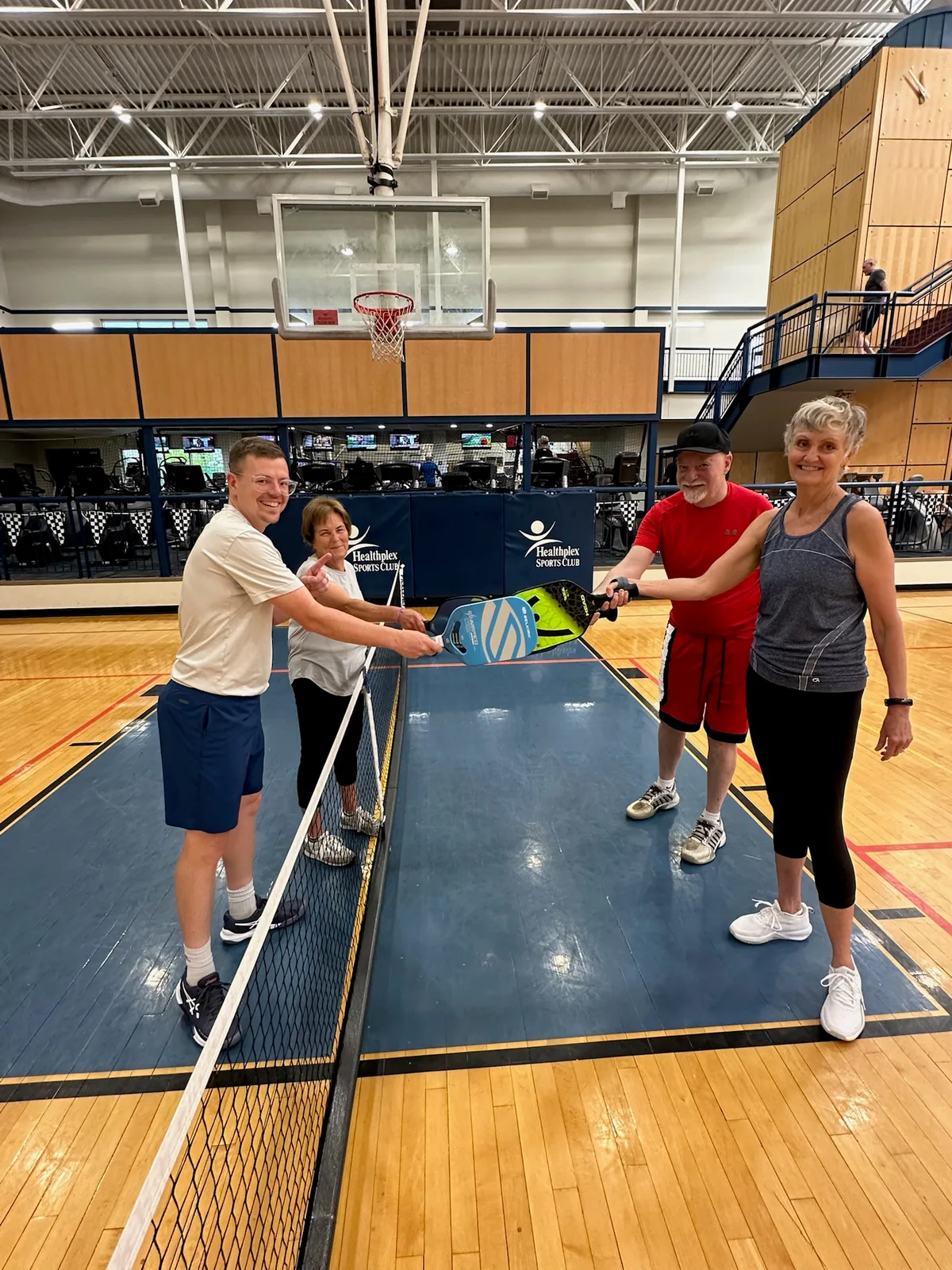 Players touching paddles across an indoor pickleball net at Indianapolis Healthplex